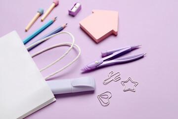 Composition with paper bag and different stationery on lilac background