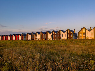 Fototapeta na wymiar Rows of newly built colorful townhouses for sale in suburbia at summer sunset. Wide angle