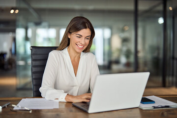 Happy cheerful mid aged business woman executive in office using laptop at work, smiling...