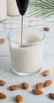 Making milk foam from vegan almond drink with automatic rotating milk frother, speed up video clip, using milk foam maker to prepare foam for coffee drinks, 4k footage, vertical clip for social media
