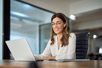 Happy mid aged business woman having hybrid meeting working in office. Busy mature female corporate leader executive, hr manager communicating by conference call, remote online job interview on laptop
