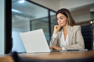 Busy mature business woman working in office using laptop. Mid aged female professional businesswoman executive manager wearing suit looking at computer thinking on digital strategy, sitting at desk.