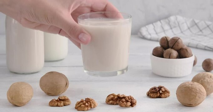 Vegan milk. Person taking a glass full of alternative milk made of walnuts, hand grabbing a glass from white wooden table, non-dairy product, 4k horizontal video, slow motion footage