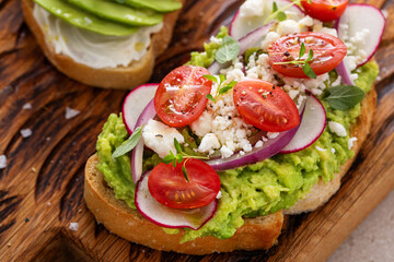 Avocado toasts with radishes, tomatoes and feta topped with olive oil