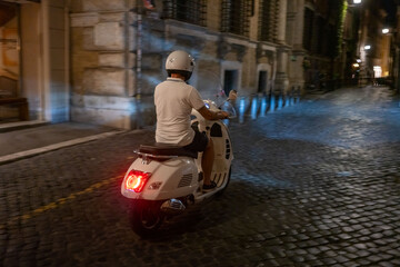 Man rides Italian motor scooter rides down small roman street at night in Rome, Italy  © Mustard Assets