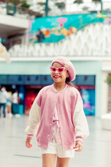 Retrato de linda niña sonriente con atuendo rosa y gafas  de sol rosa en el centro comercial.