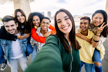Young group of diverse students having fun together outdoors. Beautiful woman smile at camera taking selfie portrait with diverse friends on the background. Youth community concept. - obrazy, fototapety, plakaty