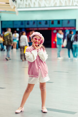 Retrato de linda niña sonriente con los brazos levantados y estilo unico con atuendo rosa y gafas de sol rosa 