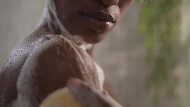 African American woman cleaning her skin sponge relaxing in shower from shoulder to face. Close-up of black afro adult female using soap for daily hygiene. Personal body care in bathroom at home. 