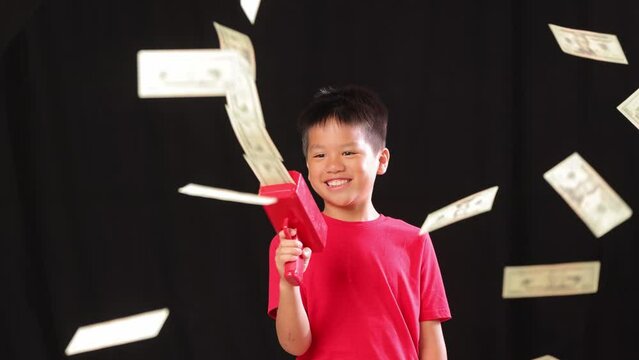 10 year old Asian boy shooting money out of a money gun. Slow Motion.