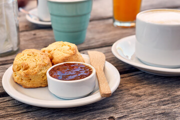 Traditional British scones on a white plate, a jar of strawberry jam and a cup of coffee, latte. Breakfast, tea time concept.