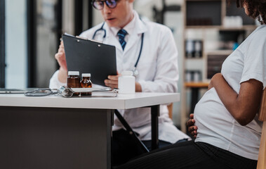 Male gynecologist doctor checking african american pregnant woman, Gynecology Consultation concept, examining belly stethoscope, obstetrician OB doctor special training in women health and pregnancy