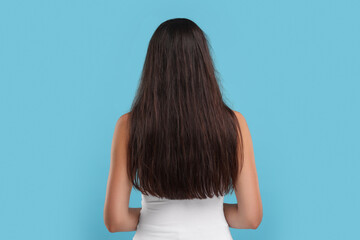 Woman with damaged messy hair on light blue background, back view