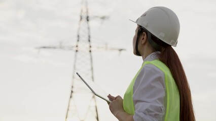 Woman engineer works on tablet by electric power transmission line support