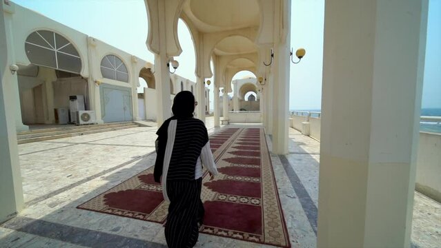 A girl in black and white arabic clothing walking on a carpet in a place with arches, in a mosque near the Red Sea in Jeddah, Saudi Arabia. 