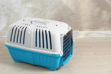 Light blue pet carrier on floor near beige wall, space for text