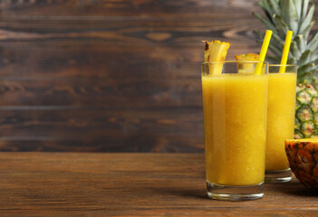 Tasty pineapple smoothie on wooden table, space for text