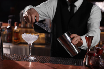 Bartender preparing fresh alcoholic cocktail in martini glass at bar counter, closeup