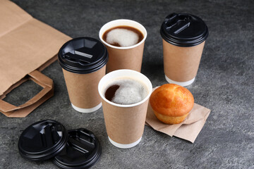 Coffee to go. Paper cups with tasty drink and muffin on grey table