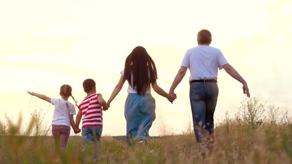 Family with little children plays plane and runs across meadow grass at sunset