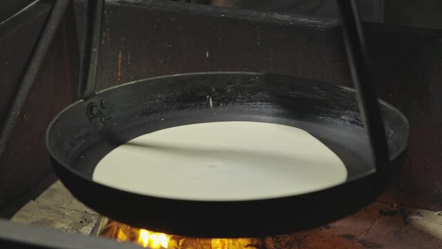 Pouring pancake batter on pan over fire