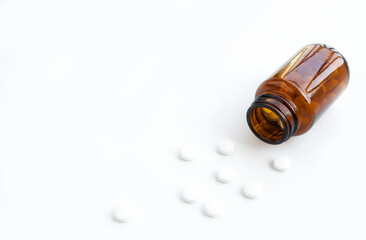 White pills spilling out of brown glass bottle on white background. Medicine, healthcare 