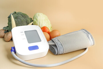 Automatic blood pressure monitor on beige colored background. Digital blood pressure monitor and fresh vegetables on beige background with copy space. health care and medical concepts