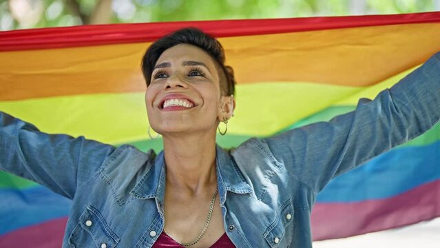 Young beautiful hispanic woman smiling confident holding rainbow flag at park
