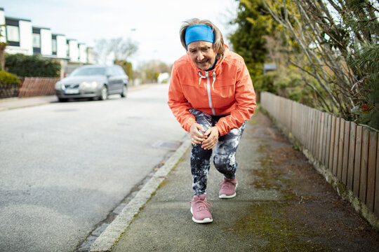 Senior caucasian woman getting her knee joint injured while jogging and exercising in the suburbs