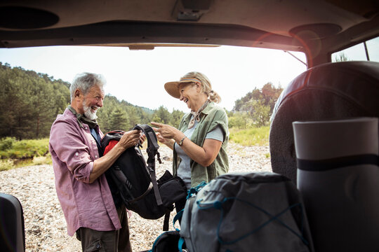 Senior couple taking equipment out of their car trunk and getting ready to go hiking in the forest and mountains