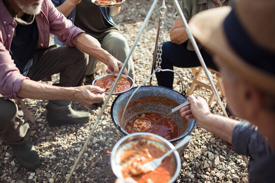 Group of senior people camping and cooking up a fish stew after a long day of hiking in the mountains and forests