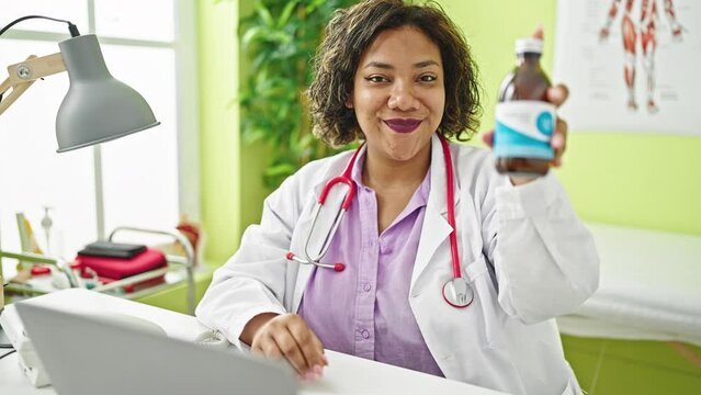 Young beautiful latin woman doctor using laptop holding medication bottle at clinic