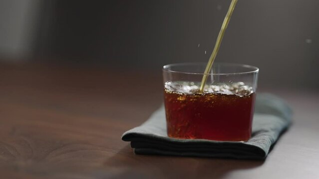Slow motion pour nitro coffe in tumbler glass on wood table