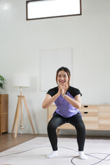 Fototapeta premium Young asian woman doing exercise with workout squatting on the floor for healthy lifestyle at home