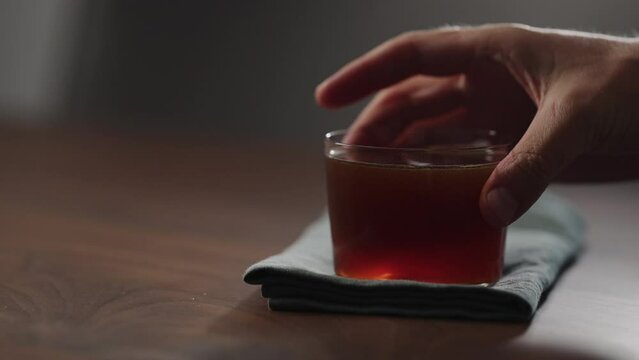 Slow motion man hand take nitro coffe in tumbler glass on wood table