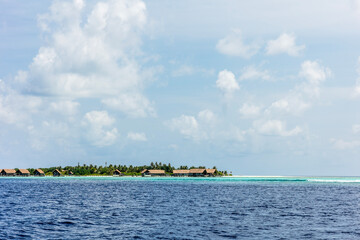 Fototapeta na wymiar Small huts in the middle of ocean with blue and cloudy sky background. Seascape of a village.