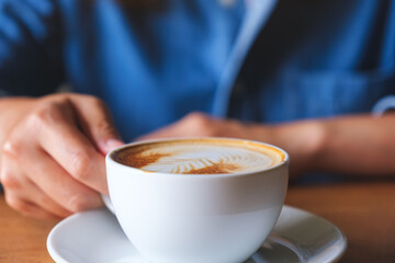 Closeup image of a woman holding a cup of latte coffee on the table
