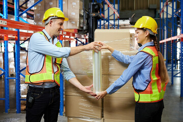 factory workers or warehouser wrapping stretch film parcel on pallet covered cardboard boxed in warehouse storage