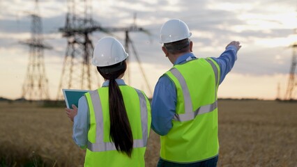 Engineer with tablet presents power plant project to manager walking along field
