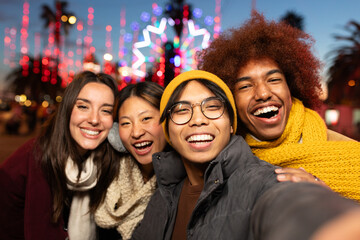 Multiracial friends laughing and having fun together taking selfie during winter Christmas market...