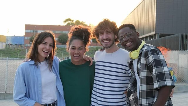 Group of happy and smiling multiracial friends embracing looking at camera standing outdoors during sunset. Slow motion.