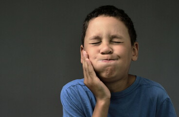 child suffering from toothache holding his jaw on the grey background with people stock image stock...