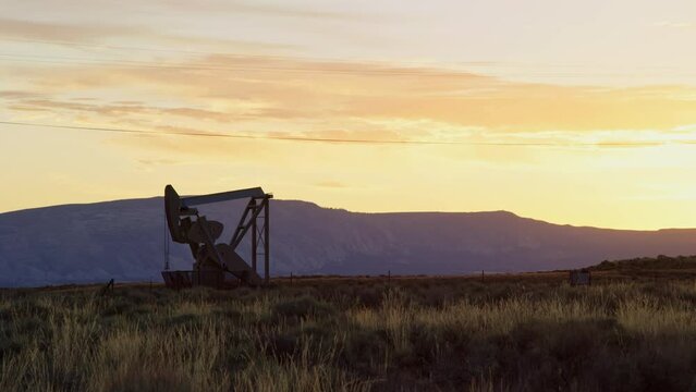 Oil pump works in large desert field as sun rises over beautiful Utah mountains