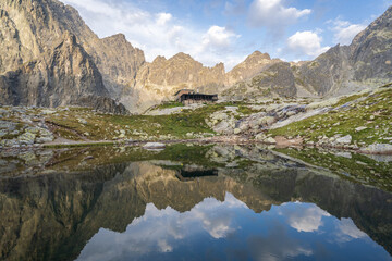 Fototapeta na wymiar Alpine hut surrounded by mountains reflected in foreground tarn during sunrise, Slovakia, Europe