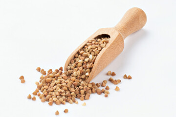 Wooden scoop of roasted buckwheat on a white background.