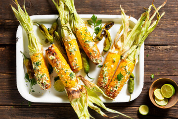 Grilled corn cobs with butter, parsley and Shishito pepper, on a tray, wooden background. Top view.