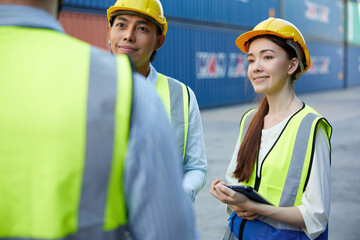 factory worker or engineer holding tablet and talking with coworker in containers warehouse storage