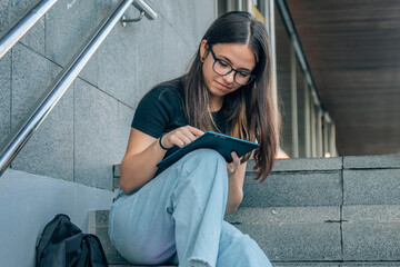 student teen girl with tablet on the stairs of college or campus
