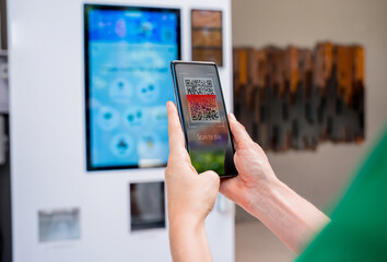 Young woman paying for coffee at vending machine using contactless method of payment 