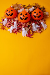 Overhead view of orange Halloween pumpkins on a background of yellow, decorated with red autumn leaves and little ghosts, copy and paste space